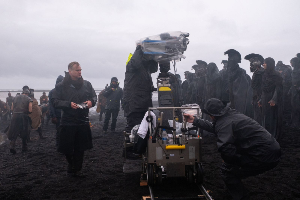 Director Christopher Nolan on set of his film THE ODYSSEY standing on a black sand beach in Iceland.